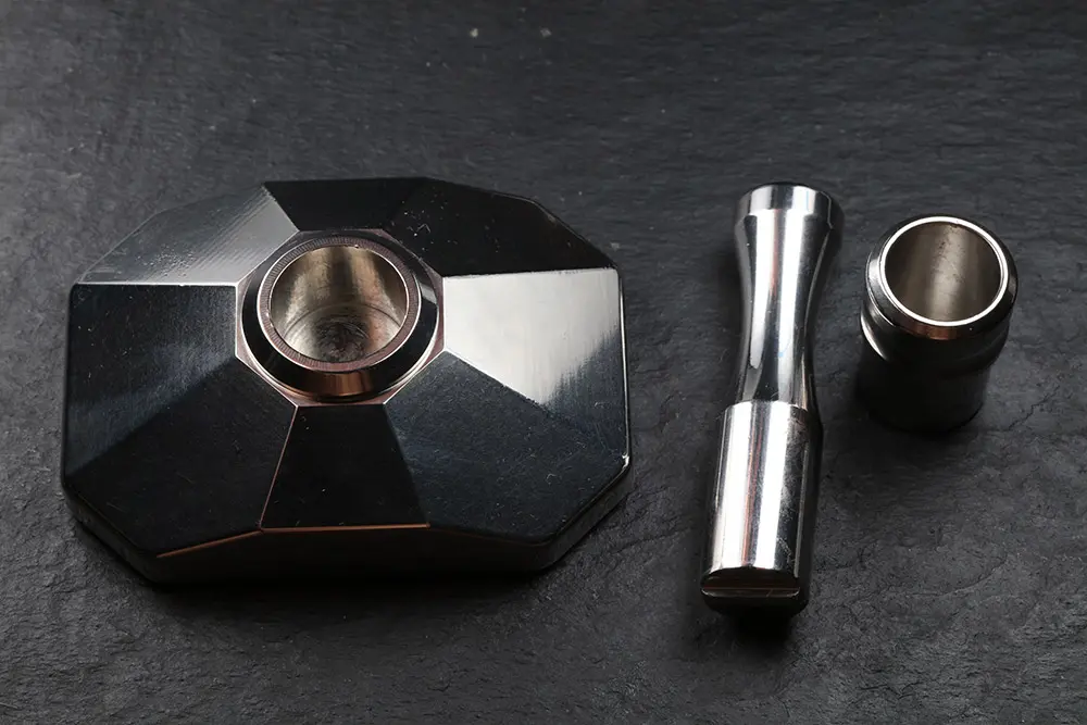 The three pieces on dark slate: the faceted base with the cup seated in it, the pestle and a second cup